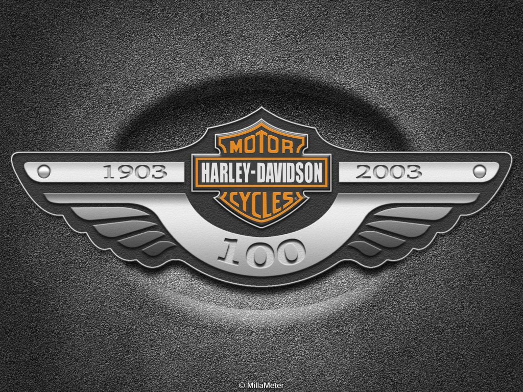 Harley-Davidson 100th Anniversary wing emblem metallic badge on dark textured wallpaper background