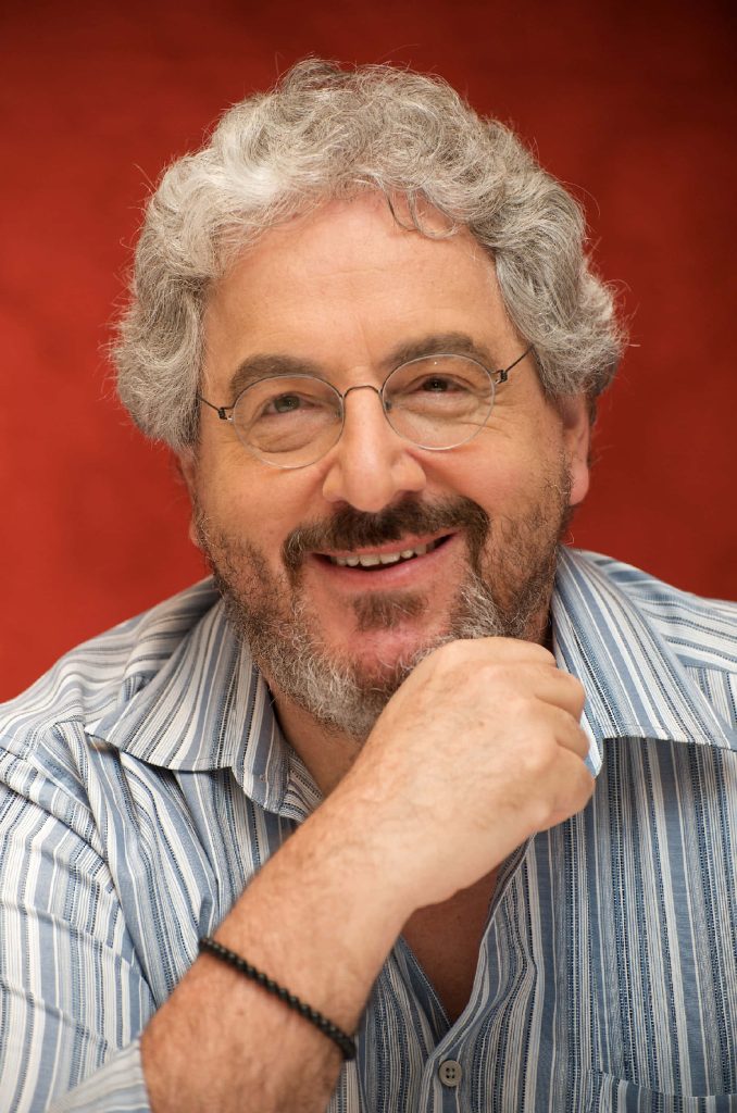 Close-up portrait of Harold Ramis smiling with round glasses blue striped shirt red background Wallpaper