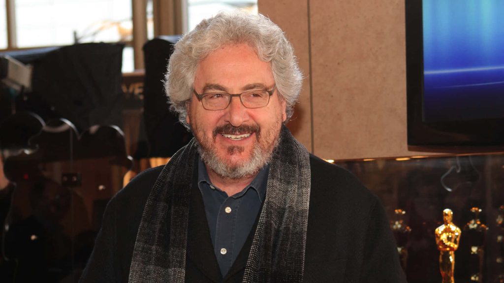 Portrait of Harold Ramis with curly grey hair glasses dark coat and plaid scarf wallpaper