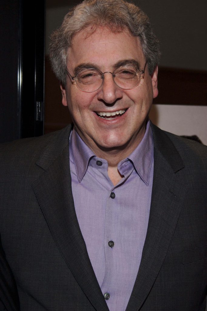 Portrait of late filmmaker Harold Ramis wearing glasses dark blazer and lavender shirt smiling Wallpaper