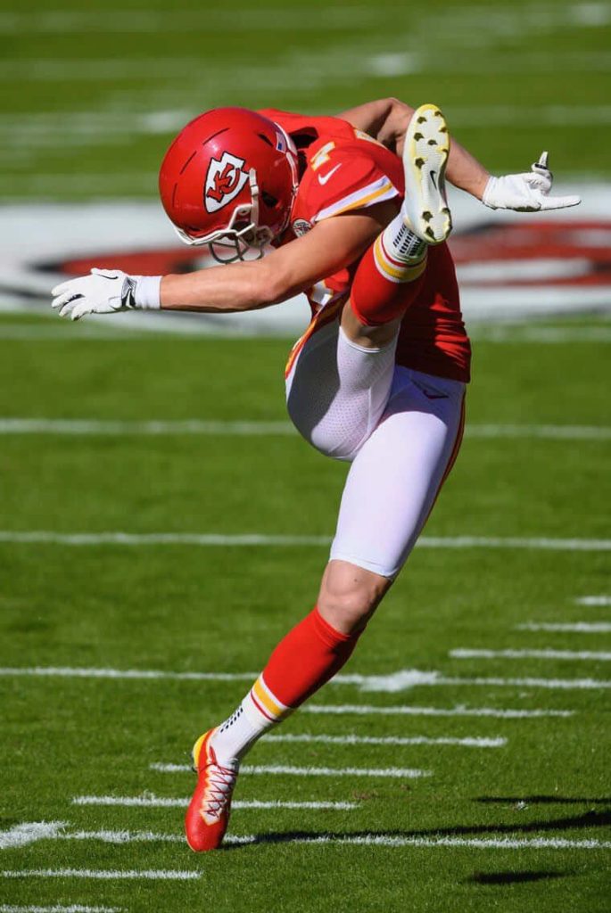 Kansas City Chiefs kicker Harrison Butker in mid kick wearing red and white uniform on green field Wallpaper