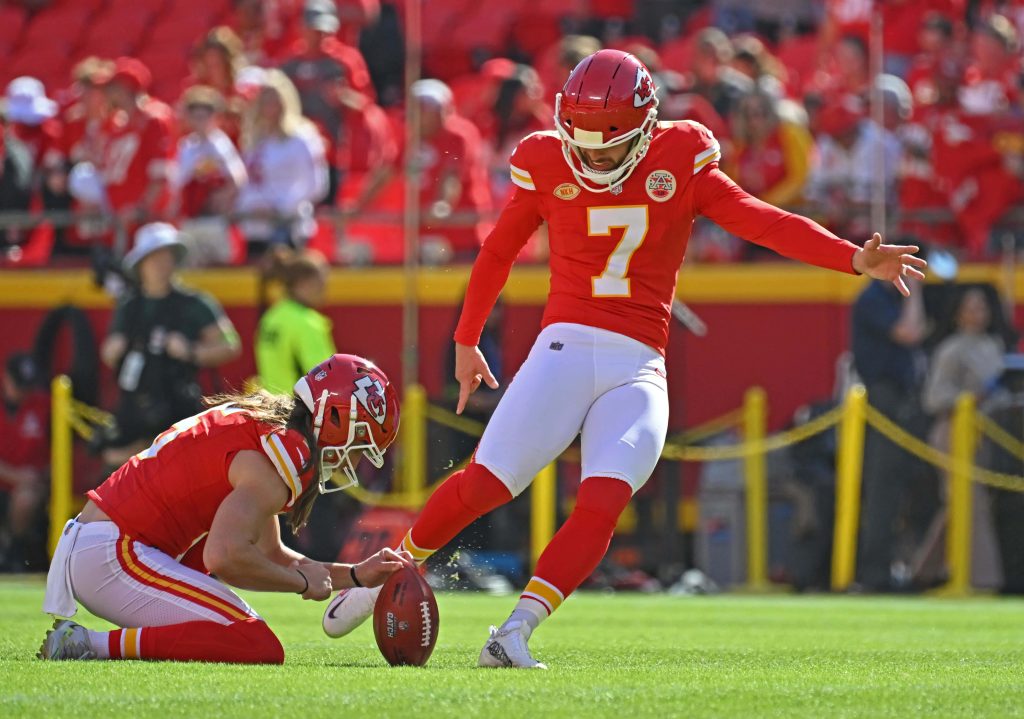Kansas City Chiefs kicker Harrison Butker attempts field goal held by Tommy Townsend on green field Wallpaper
