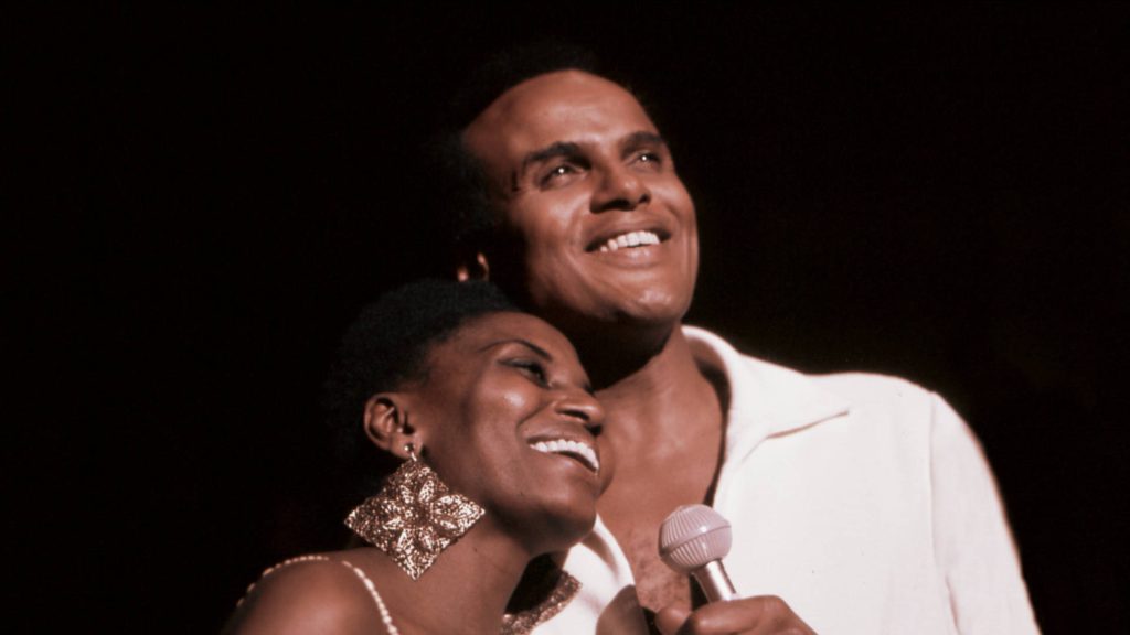 Harry Belafonte and Miriam Makeba performing live under warm stage lights in soulful harmony Wallpaper