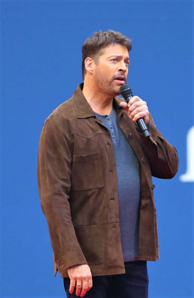 Harry Connick Jr. speaking into microphone in brown suede jacket on solid blue background wallpaper