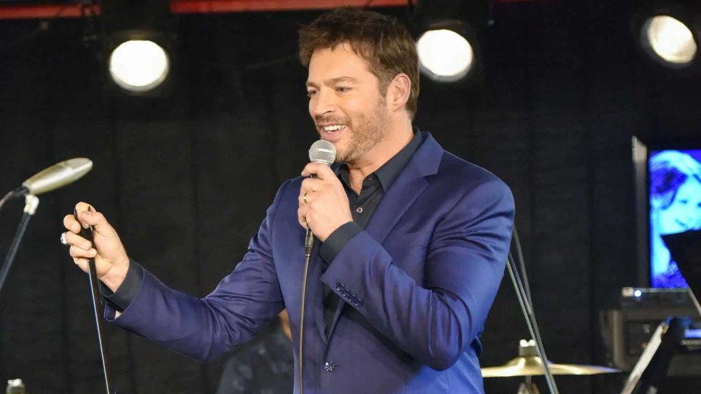 Harry Connick Jr. onstage in navy blazer singing with microphone at dark concert venue lights Wallpaper