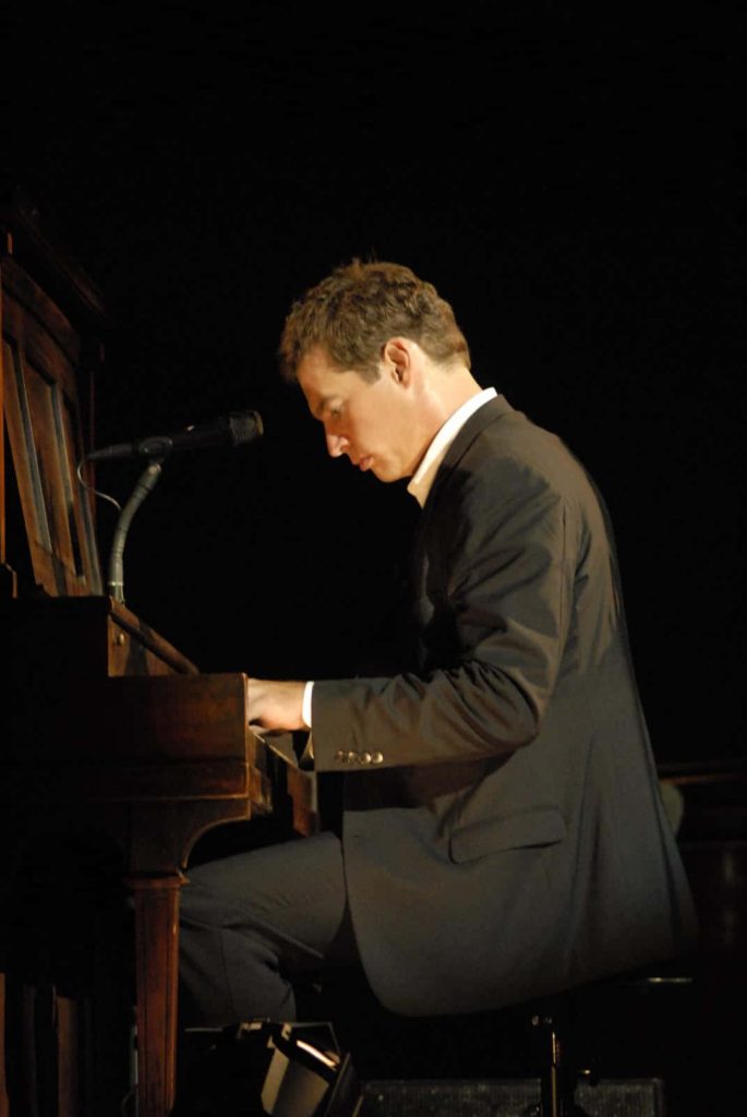 Harry Connick Jr playing piano in dark suit under dramatic stage lighting wallpaper background