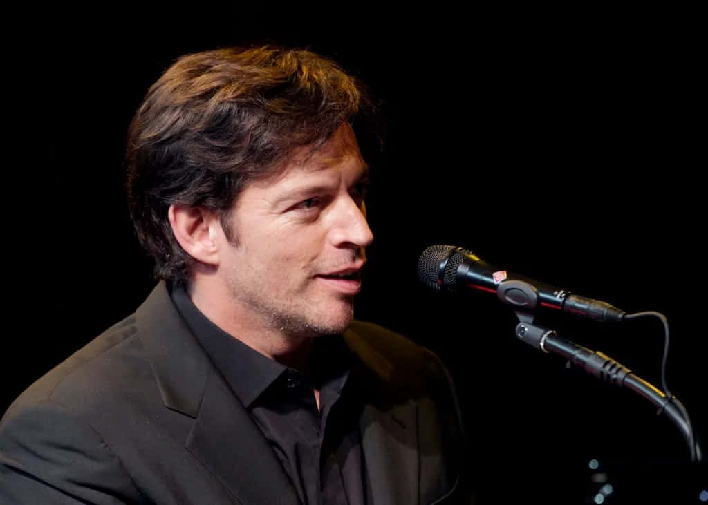 Harry Connick Jr in black suit mid-performance singing into microphone dark background Wallpaper