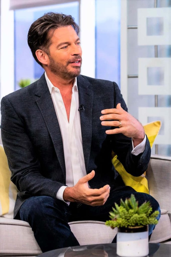 Harry Connick Jr. in charcoal blazer mid-interview on bright studio couch modern TV set wallpaper