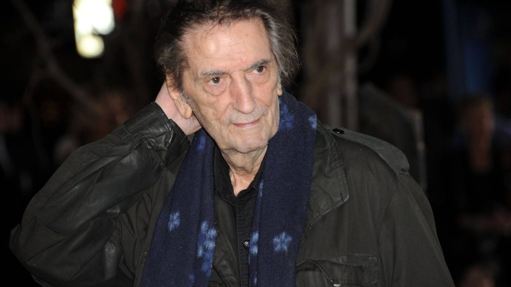 Harry Dean Stanton candid portrait wearing dark jacket and blue scarf in high-contrast lighting Wallpaper
