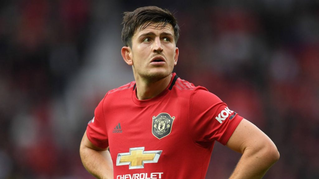 Harry Maguire in red Manchester United kit focused on pitch with stadium lights background Wallpaper