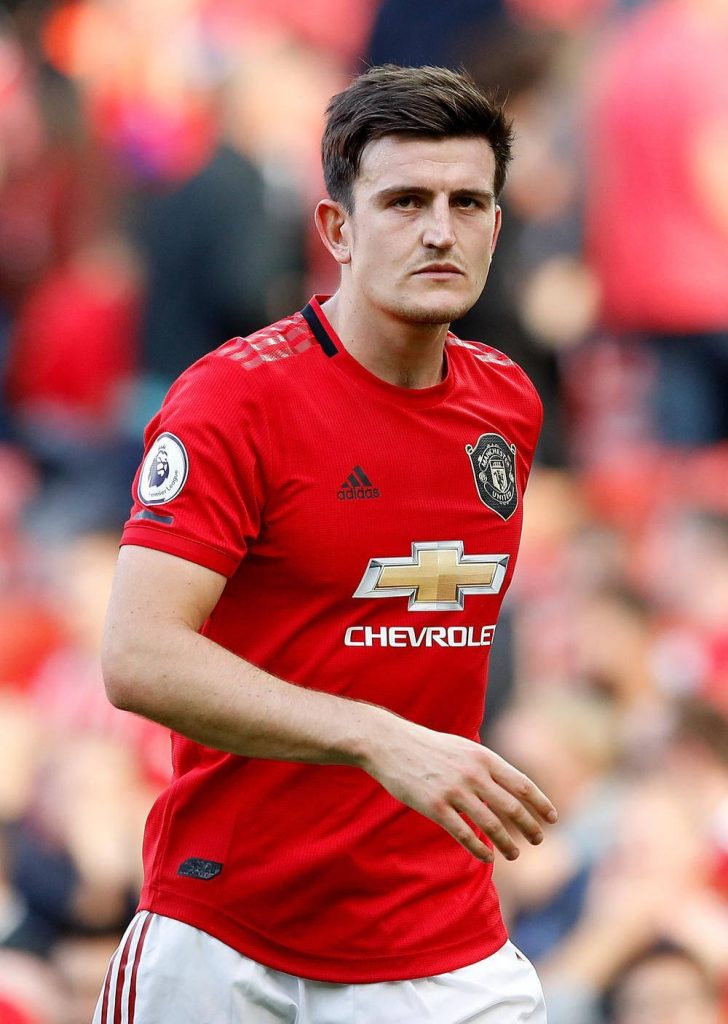 Harry Maguire in red Manchester United kit focused during match with blurred stadium background Wallpaper
