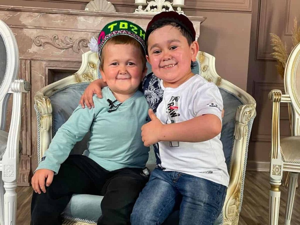 Hasbulla Magomedov and Abdu Rozik smiling together seated on ornate chair warm indoor wallpaper