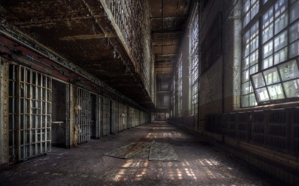 Abandoned prison corridor with rusted cells and shattered windows illuminated by natural light Wallpaper