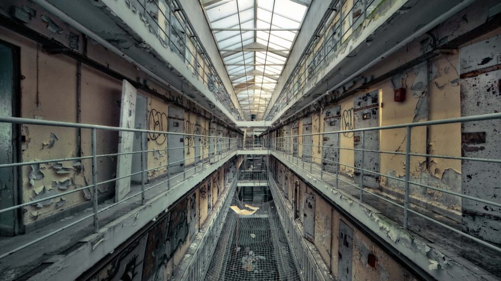 Haunting abandoned prison interior with symmetrical cell block peeling paint graffiti skylight light Wallpaper