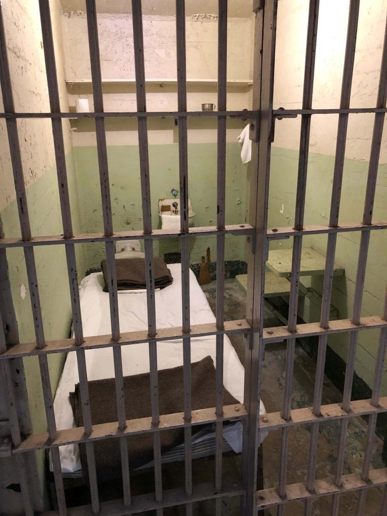 Haunting Alcatraz prison cell view through metal bars with vintage plumbing and peeling walls Wallpaper