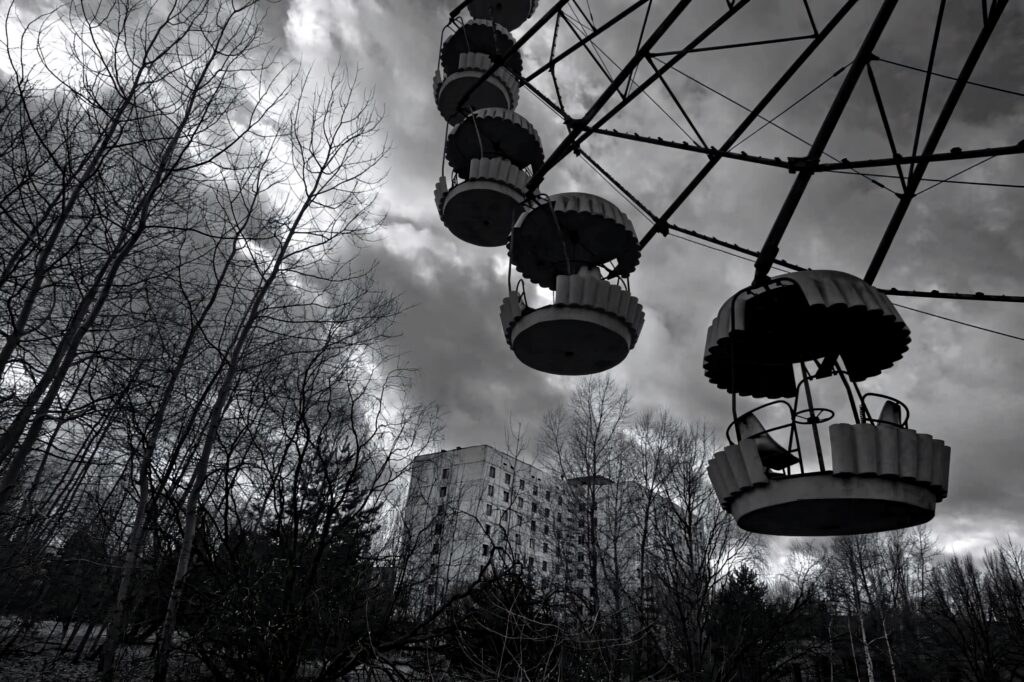 Abandoned rusted Ferris wheel in Chernobyl forest with old apartment block under cloudy sky Wallpaper