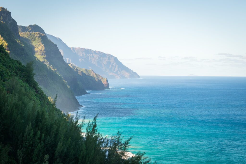 Hawaii rugged mountains above blue ocean with lush greenery and soft sunlight wallpaper background