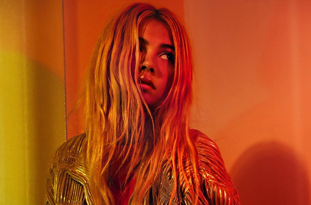 Hayley Kiyoko portrait in metallic gold jacket with warm sunset lighting vibrant orange background Wallpaper