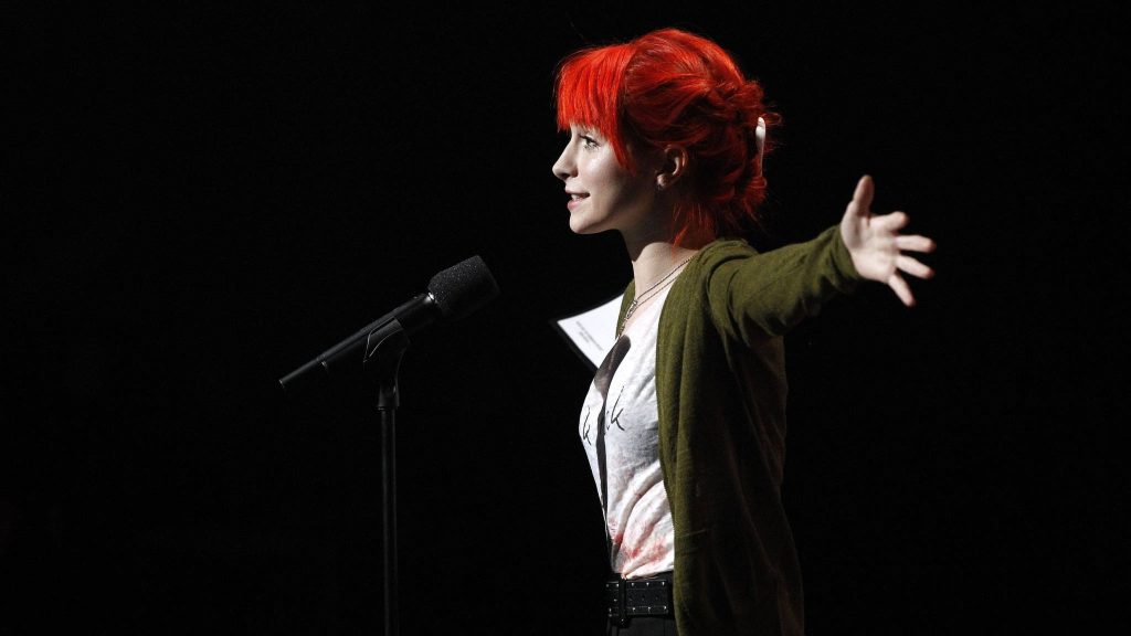 Hayley Williams Paramore lead singer with vibrant red hair singing on stage black background wallpaper