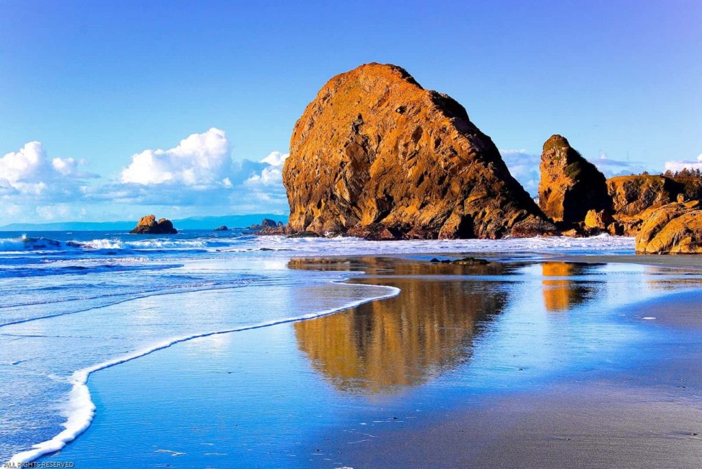 Haystack Rock at Cannon Beach Oregon glowing in sunlight with reflection on wet sand coastal wallpaper