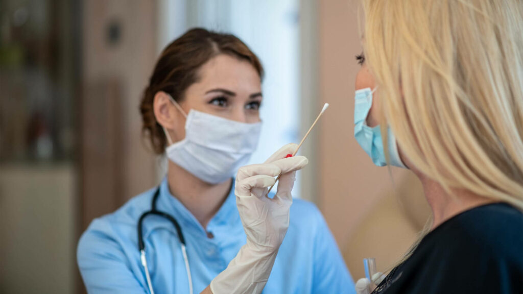 Healthcare worker in blue uniform and mask administering swab test in calm clinical setting Wallpaper
