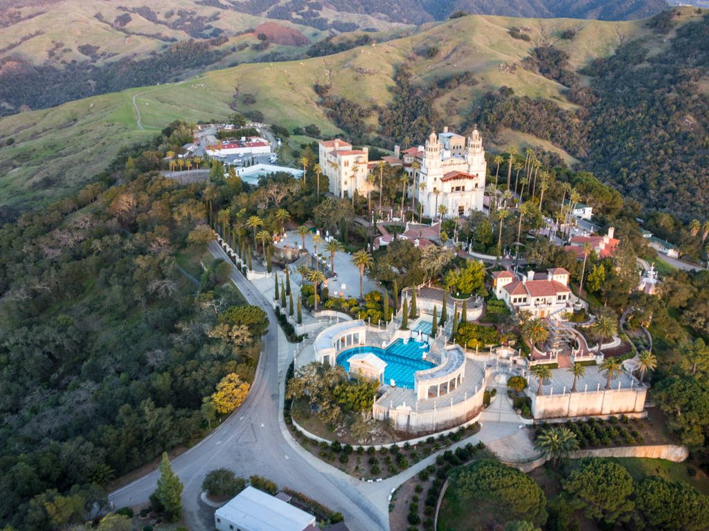 Aerial view of Hearst Castle with Neptune Pool and lush San Simeon hills under sunlight Wallpaper