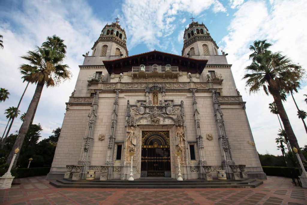 Worm's-eye view of Hearst Castle Casa Grande facade with palm trees and blue sky background Wallpaper