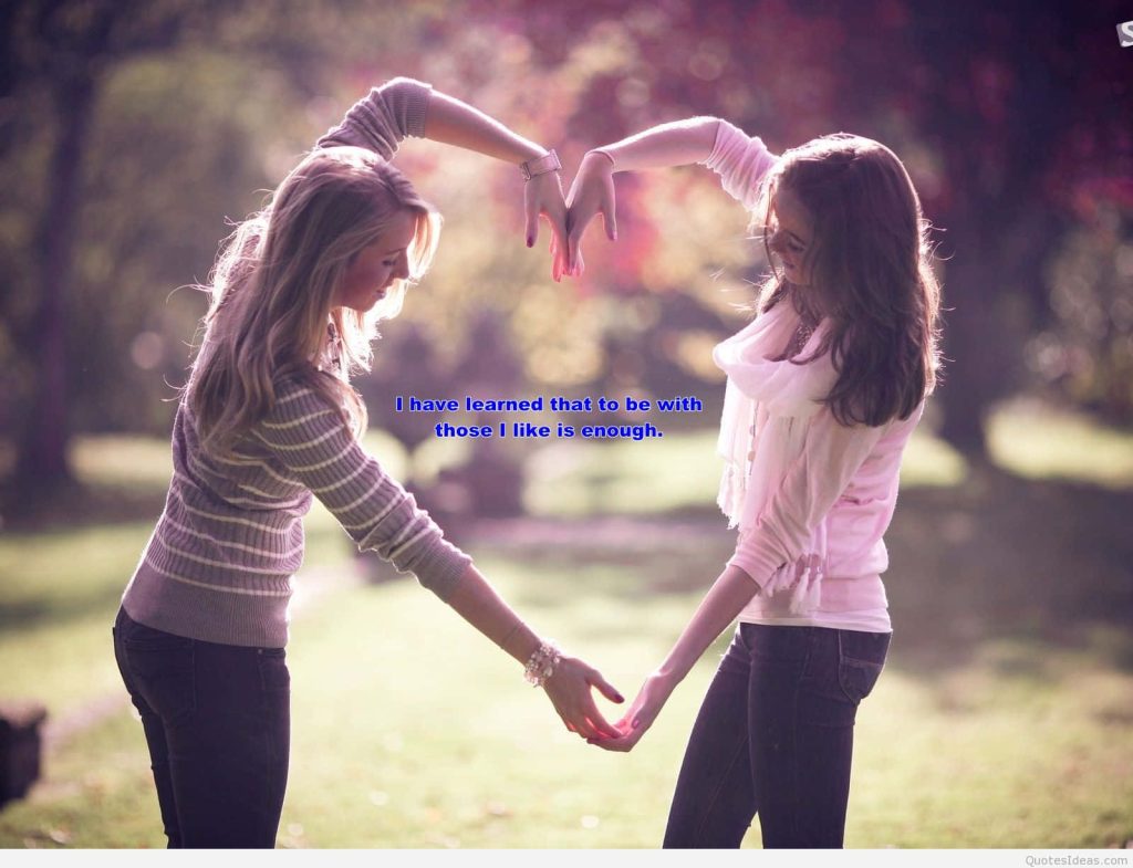 Two friends in sunlit park making heart shape with arms soft bokeh background friendship quote Wallpaper