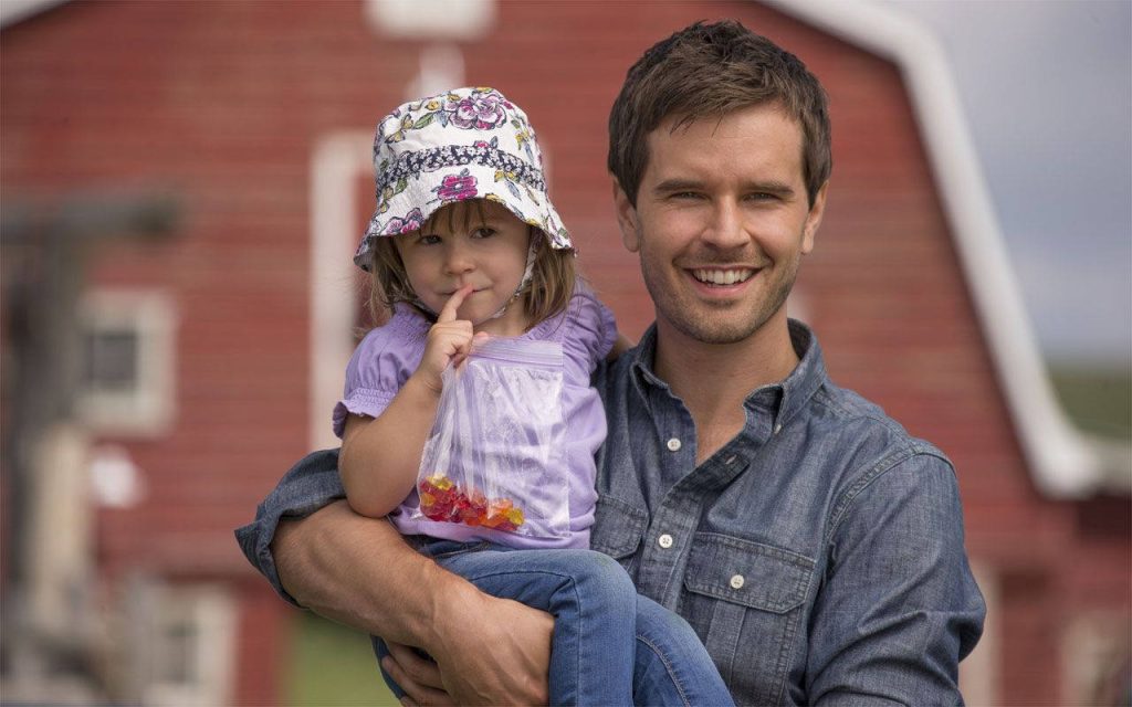 Graham Wardle carrying smiling girl in front of rustic red barn Heartland farm wallpaper background