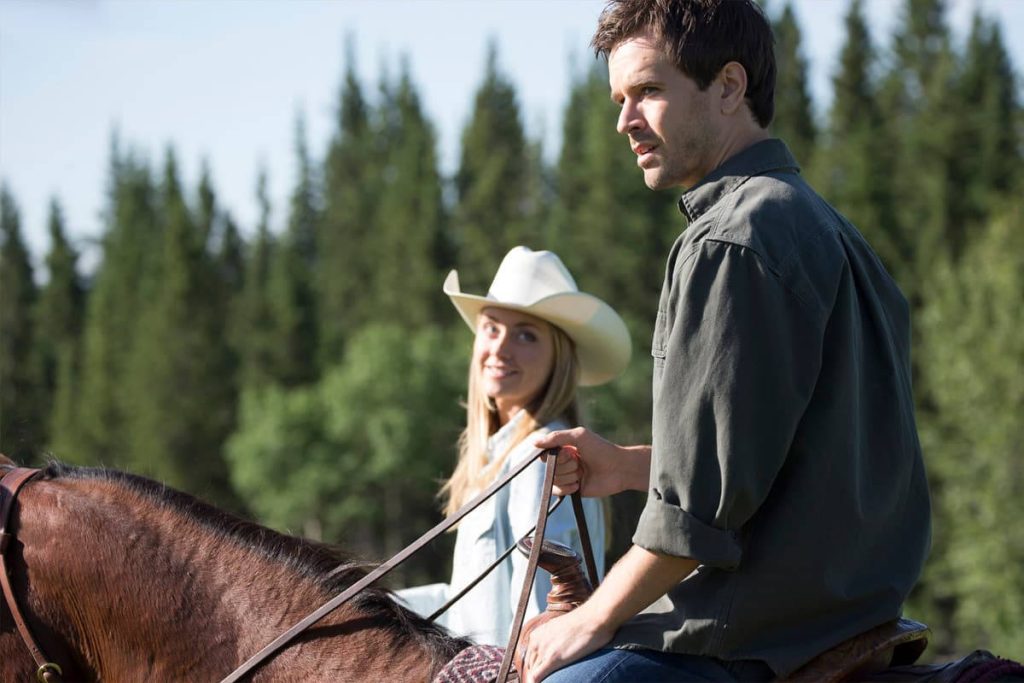 Graham Wardle and Amber Marshall horseback ride in sunlit pine forest Heartland wallpaper background