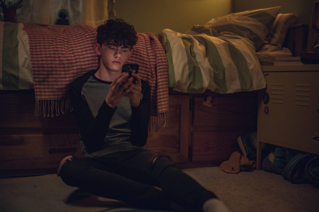 Heartstopper wallpaper Joe Locke as Charlie Spring scrolling phone moody indoor lighting bedroom