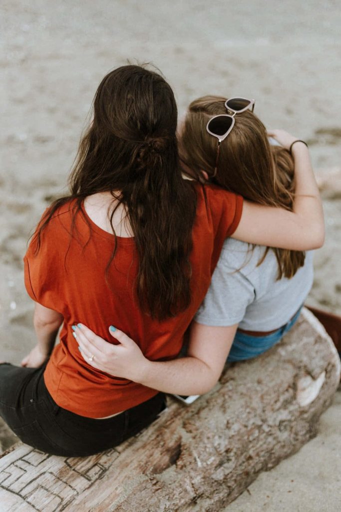 Two best friends embracing on driftwood at beach warm natural light casual friendship wallpaper