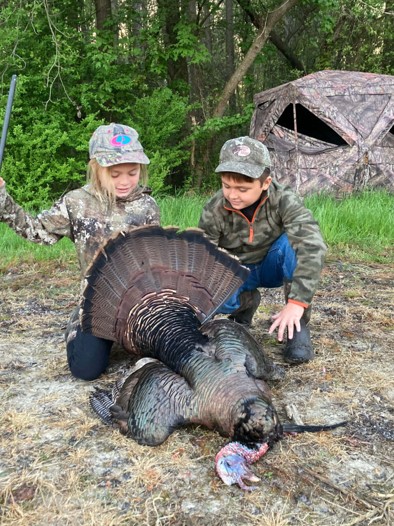 Cheerful Kids in Camouflage Pose with Turkey in Lush Forest Wallpaper
