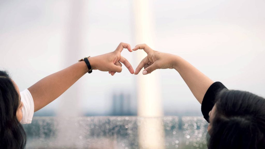 Two friends making a heart shape with hands outdoors bright natural light peaceful wallpaper background
