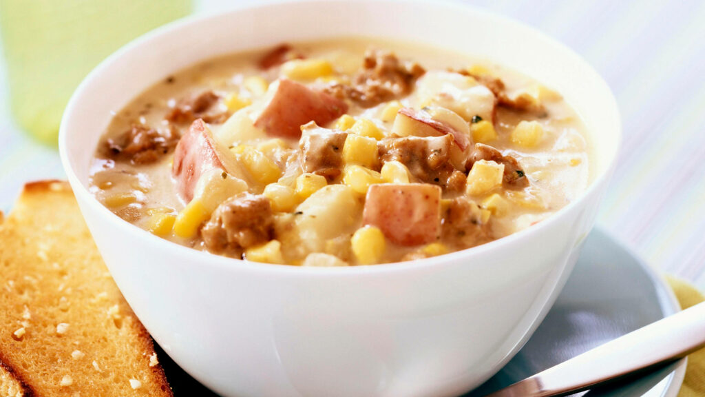 Steaming bowl of hearty beef chowder with corn potatoes creamy broth and toasted bread side Wallpaper