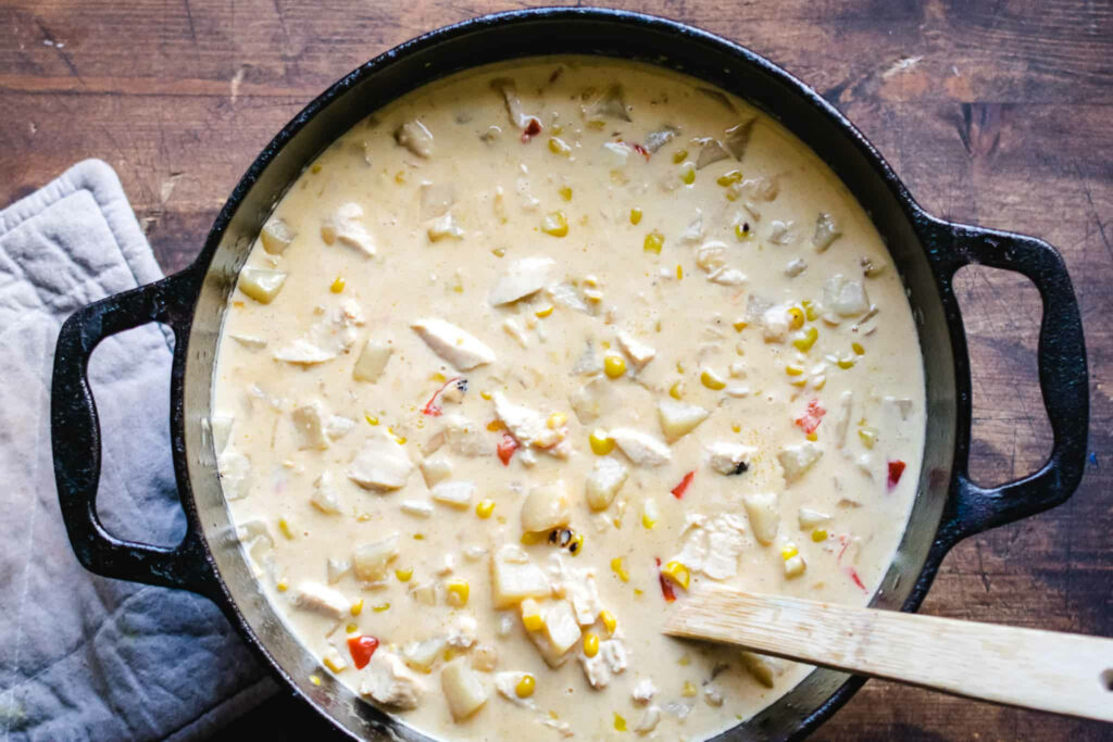 Hearty cheesy chicken chowder with corn potatoes and vegetables in cast iron pot on wood Wallpaper