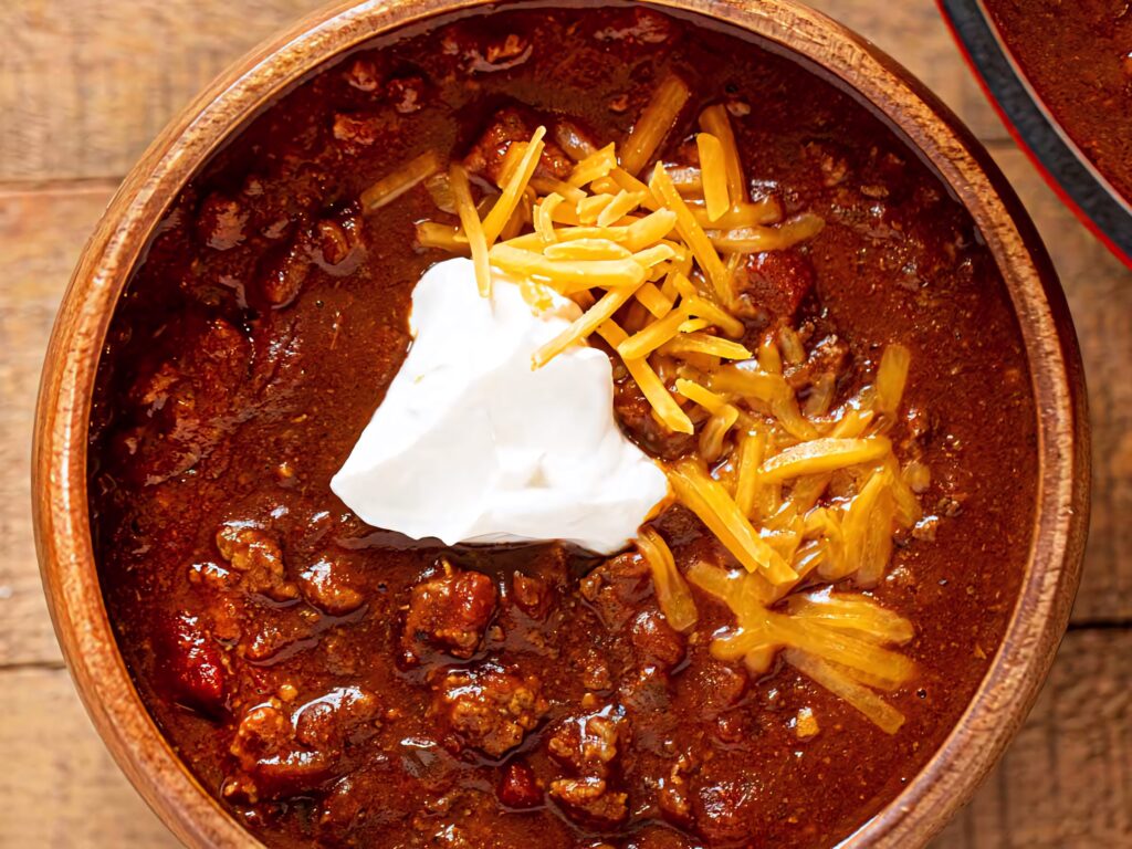 Hearty chili con carne bowl with melted cheese sour cream vibrant spicy comfort food wallpaper