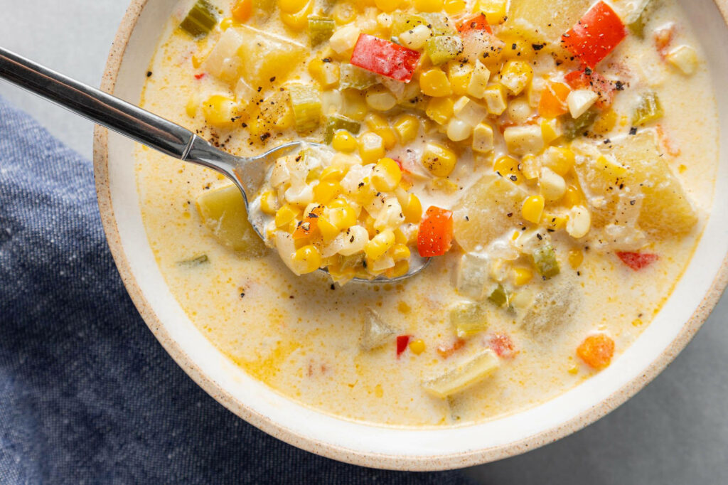 Vibrant bowl of creamy corn chowder with potatoes and bell peppers on rustic wallpaper background