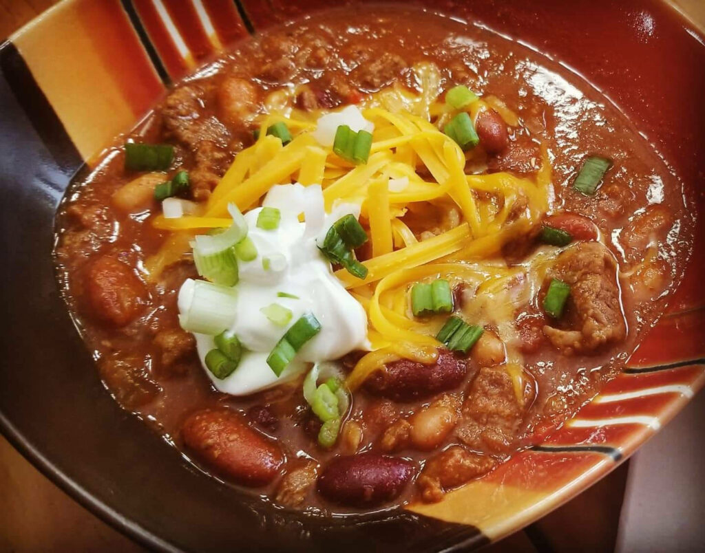Hearty bowl of Mexican chili con carne with beef beans cheese green onions and sour cream wallpaper