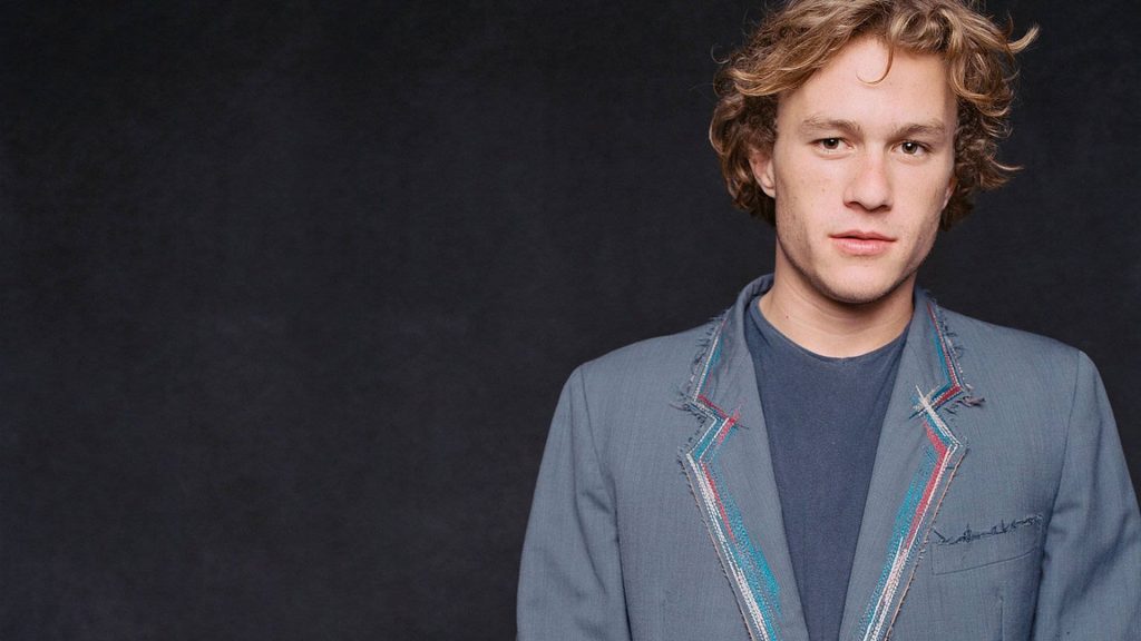 Portrait of Heath Ledger in grey blazer with colorful lapel stitching on dark background Wallpaper