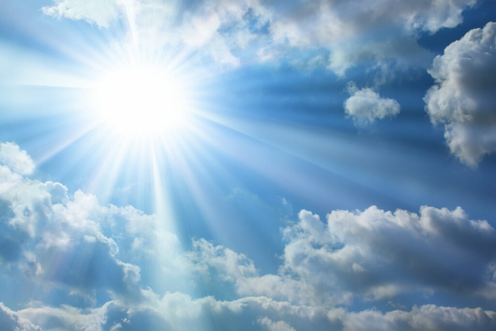 Heavenly white sunburst shines through fluffy clouds in a radiant deep blue sky wallpaper background