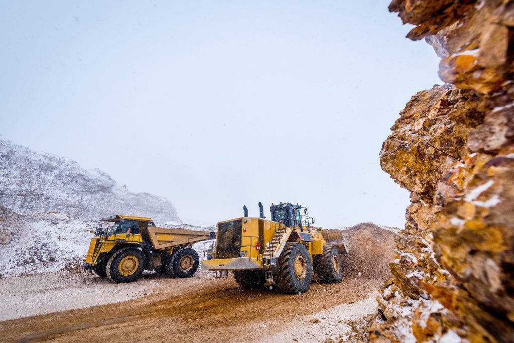 Heavy yellow wheel loader and haul truck working in snowy rugged mine under gray sky Wallpaper