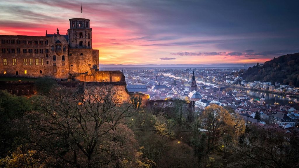 Heidelberg Castle glowing at sunset overlooking Neckar River and scenic German cityscape Wallpaper