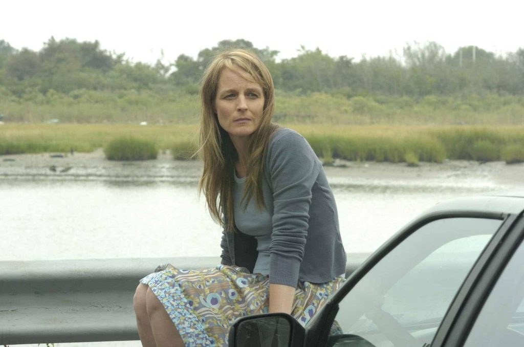 Helen Hunt in grey sweater and skirt sitting on guardrail overlooking marshy roadside in Ride film scene Wallpaper