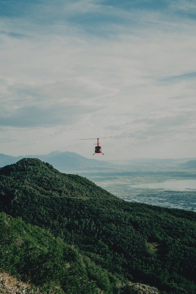 Red helicopter flying over lush green hills and forested mountain slopes scenic aerial view wallpaper