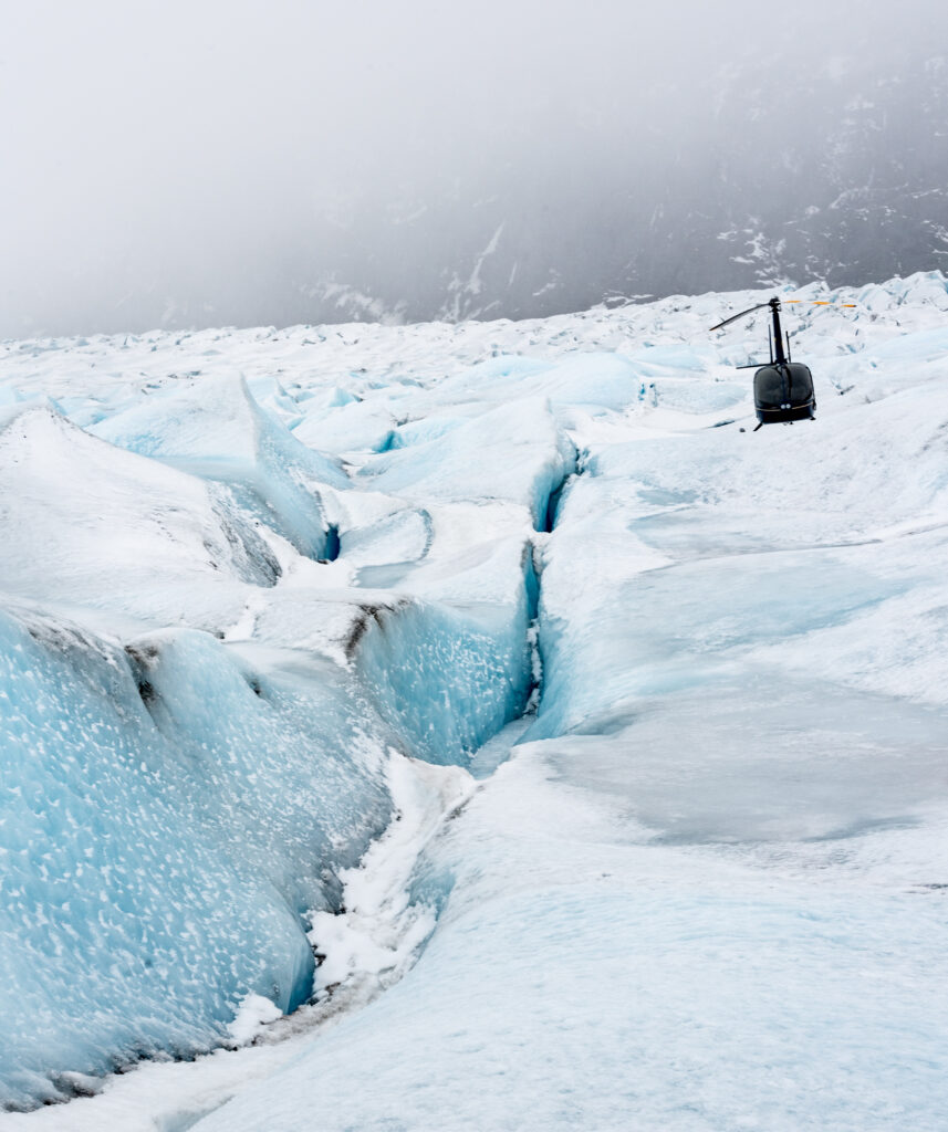 Sleek helicopter on vast glacier with rugged ice ridges snowy landscape under overcast sky Wallpaper