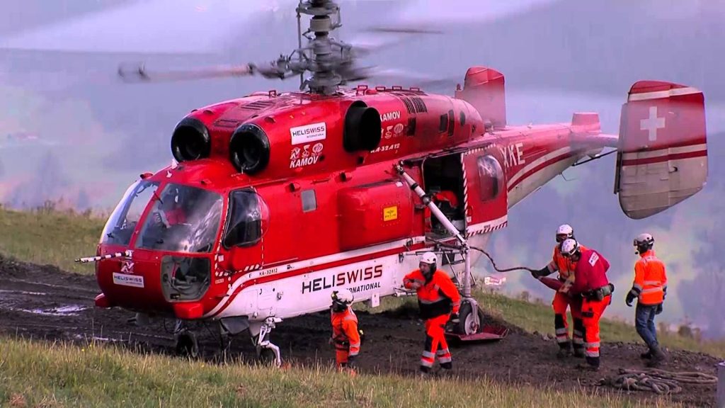 Red Heliswiss Kamov helicopter and crew in orange gear on misty mountain rescue mission wallpaper