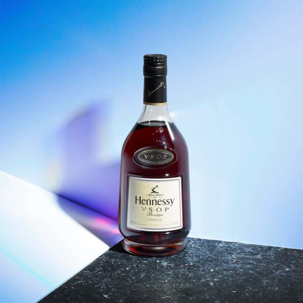 Hennessy VSOP Privilège Cognac bottle on dark stone base with blue white minimalist backdrop Wallpaper