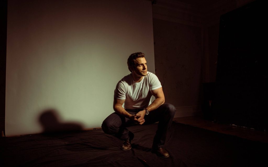 Henry Cavill crouching in white t-shirt dark jeans cinematic studio portrait dark shadow wallpaper