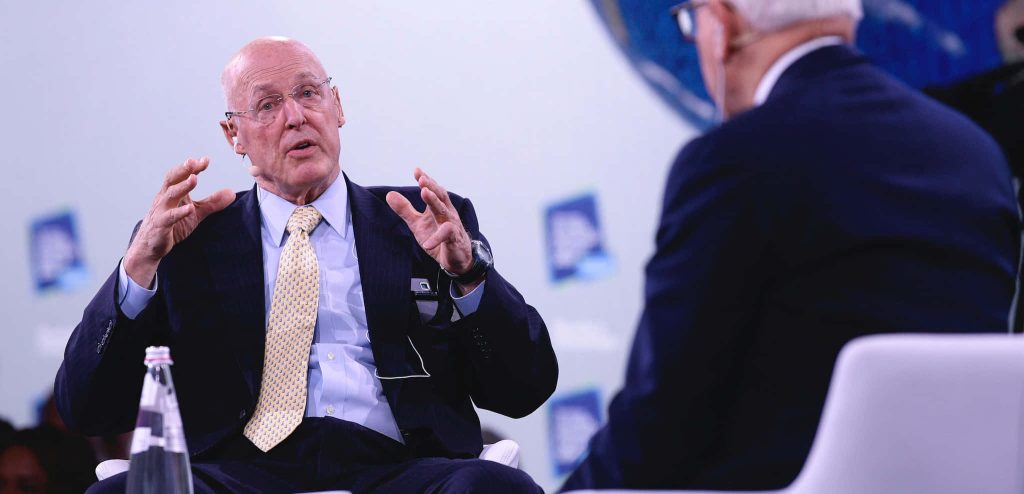 Henry M. Paulson Jr speaking at corporate panel event in dark suit and yellow tie wallpaper background